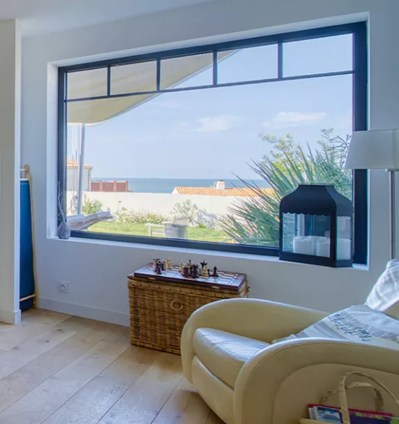 Fauteuil en cuir beige, devant une grande baie vitrée, surplombant une vue surplombant une vue sur la mer et des maisons.