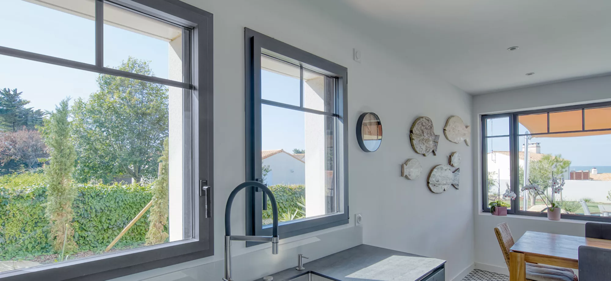 Des fenêtres laissent entrer la lumière dans une cuisine moderne, entourée d'éléments naturels et offrant une vue sur la mer.