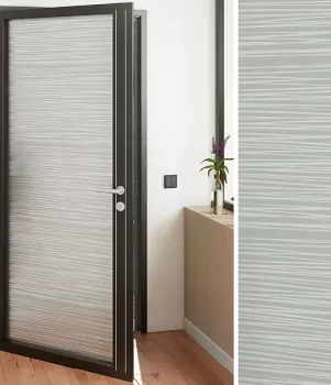 Une porte vitrée moderne s’ouvre dans un couloir en bois avec une petite table décorée d’un vase contenant des fleurs.