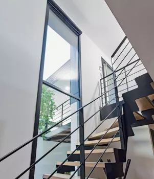Escalier moderne monte en colimaçon, encadré par des fenêtres hautes, dans un intérieur minimaliste et lumineux.