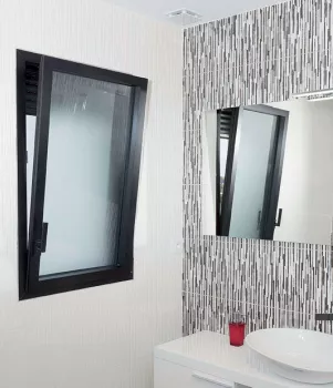 Fenêtre basculante noire s'ouvre dans une salle de bain moderne avec lavabo, miroir et carreaux muraux à motifs verticaux.
