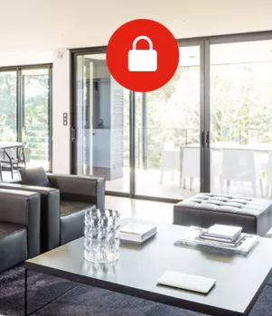 Un salon moderne comporte des canapés noirs, une table basse avec des livres et verres, et de grandes baies vitrées donnant sur une terrasse ensoleillée.