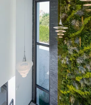 Un luminaire suspendu illumine un intérieur moderne avec une grande fenêtre et un mur végétal vertical.