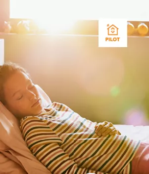 Enfant dormant paisiblement sur un lit, baigné de lumière matinale provenant d'une fenêtre ensoleillée.