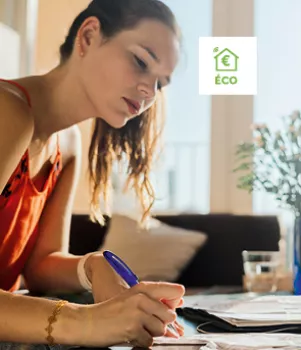 Une femme écrit sur des documents à une table, concentrée, dans une pièce lumineuse avec des plantes et un logo "éco" visible en arrière-plan.