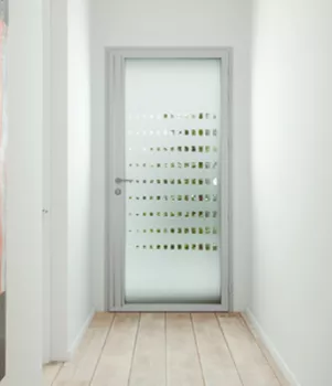 Porte en verre givré avec motifs carrés, située à la fin d'un couloir étroit, entourée de murs blancs et sol en bois clair.