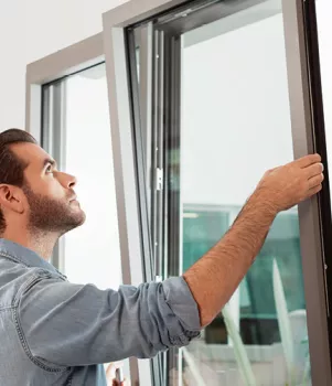Un homme ouvre une fenêtre moderne dans une maison lumineuse, examinant probablement la vue extérieure ou vérifiant l'état du cadre.