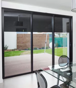 Baie vitrée donne sur un jardin avec pelouse et terrasse en bois, intégrée dans une salle à manger moderne avec table en verre et chaises en plastique transparent.