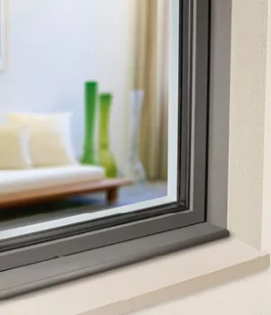 Une fenêtre noire ouverte donne sur un salon moderne avec un canapé beige et des vases verts et translucides en arrière-plan.