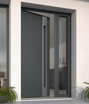 Porte moderne grise avec poignée encastrée s'ouvrant vers l'extérieur, entourée de plantes en pot, dans un encadrement de mur blanc.