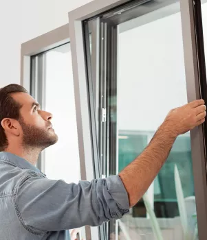 Un homme ouvre une fenêtre moderne dans une pièce lumineuse, révélant un environnement extérieur avec des plantes visibles en arrière-plan.