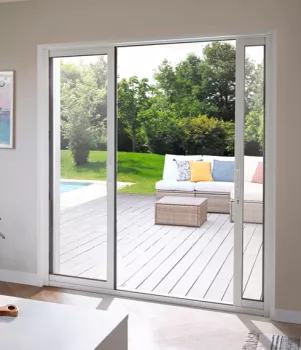 Porte coulissante vitrée donne sur terrasse ensoleillée avec canapé, table basse et jardin verdoyant en arrière-plan.