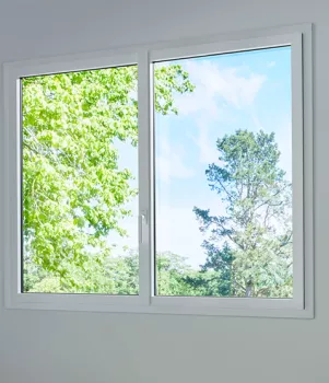 Fenêtre ouverte montrant des arbres verts et un ciel bleu, baignant la pièce de lumière naturelle.