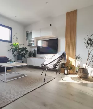 Un salon moderne avec une chaise noire, entourée de plantes vertes, illuminée par une fenêtre à gauche, décore avec des meubles blancs et des accents de bois clair.