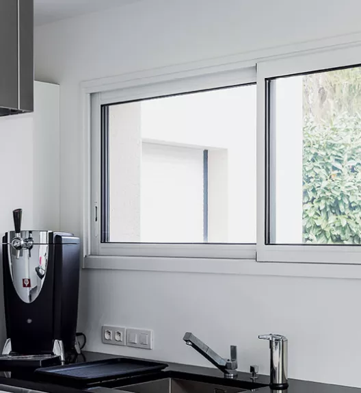 Machine à café sur un plan de travail de cuisine moderne en acier inoxydable, placée près d'une fenêtre donnant sur l'extérieur.