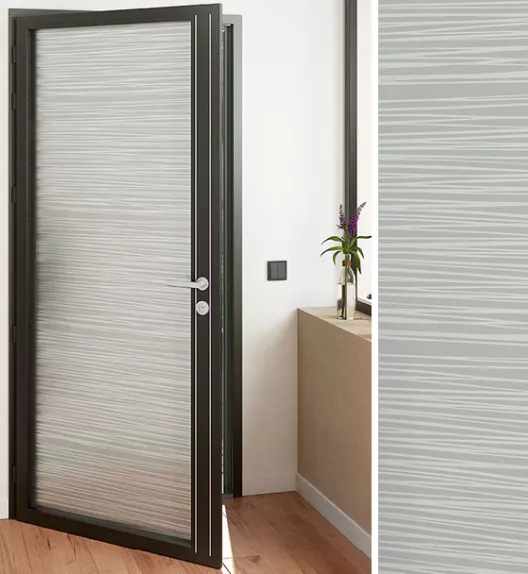 Une porte vitrée moderne s’ouvre dans un couloir en bois avec une petite table décorée d’un vase contenant des fleurs.