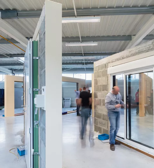 Des ouvriers installent des fenêtres et des portes dans un atelier spacieux et lumineux.