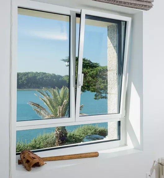 Fenêtre basculante, partiellement ouverte, offrant une vue sur un lac entouré de végétation dense, avec une batte de baseball et un gant posés sur le rebord.