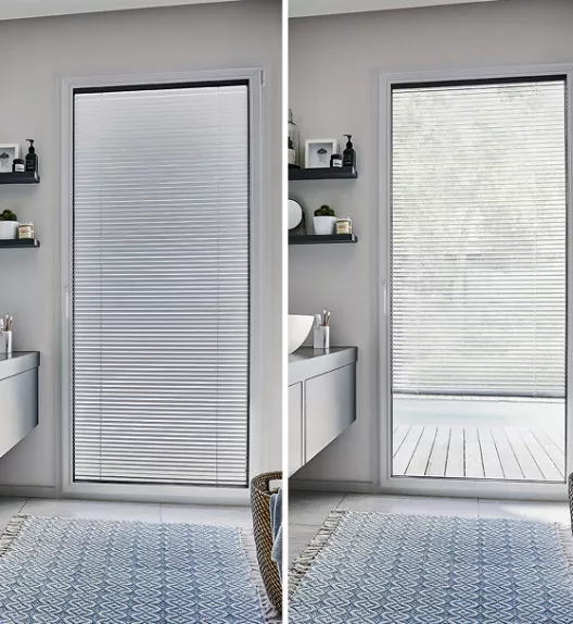 Store vénitien fermé à gauche, ouvert à droite, dans une salle de bain moderne avec meubles suspendus et tapis bleu.