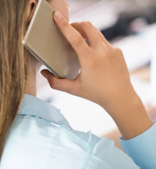 Le téléphone est tenu par une femme qui passe un appel, dans un environnement de bureau.