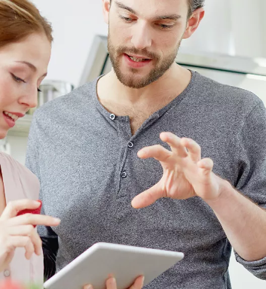 Deux personnes consultent une tablette dans une cuisine moderne, échangeant des informations et discutant activement.
