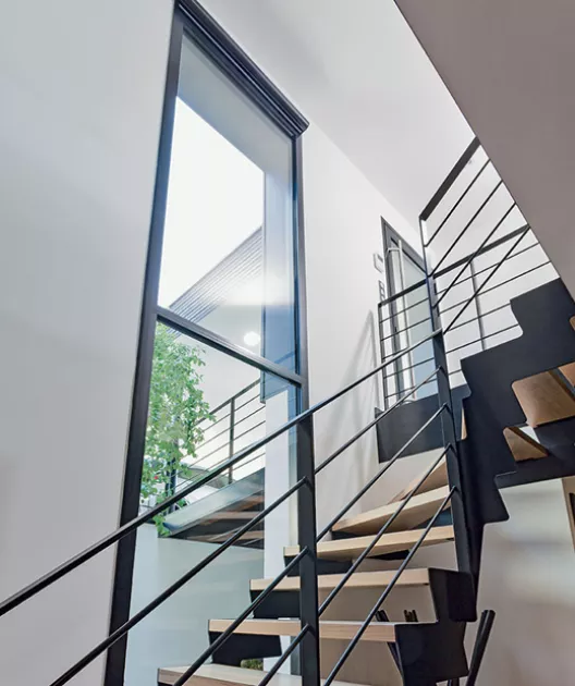 Escalier moderne monte en colimaçon, encadré par des fenêtres hautes, dans un intérieur minimaliste et lumineux.
