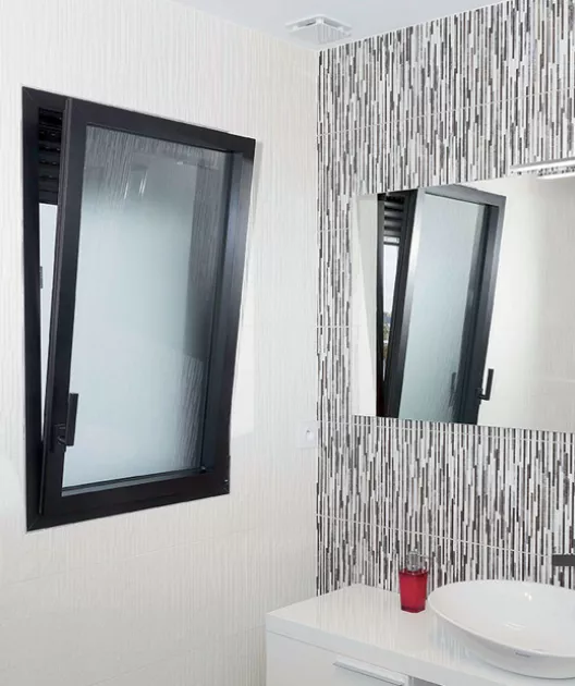Fenêtre basculante noire s'ouvre dans une salle de bain moderne avec lavabo, miroir et carreaux muraux à motifs verticaux.