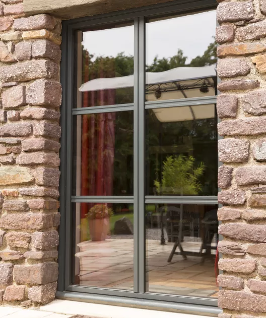 Baie vitrée coulissante à galandage encadrée de pierre montre un jardin avec une pergola blanche et des meubles de terrasse, créant une ambiance extérieure paisible.