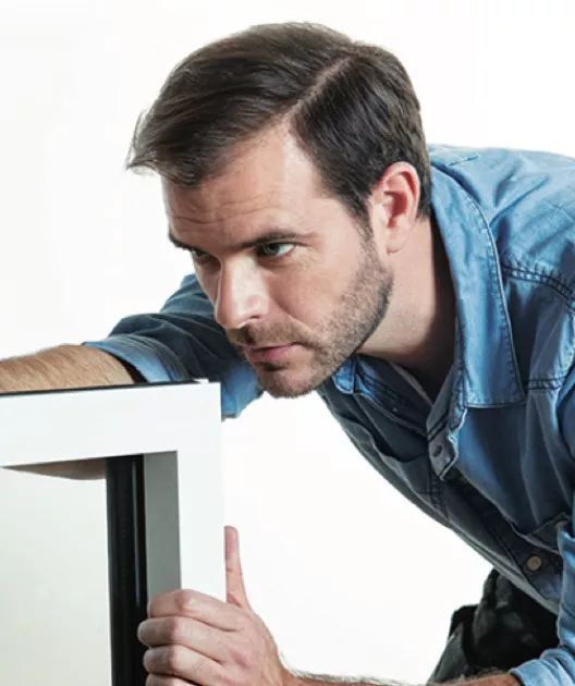 Un homme ajuste un cadre blanc, concentré sur son travail, dans un environnement intérieur.