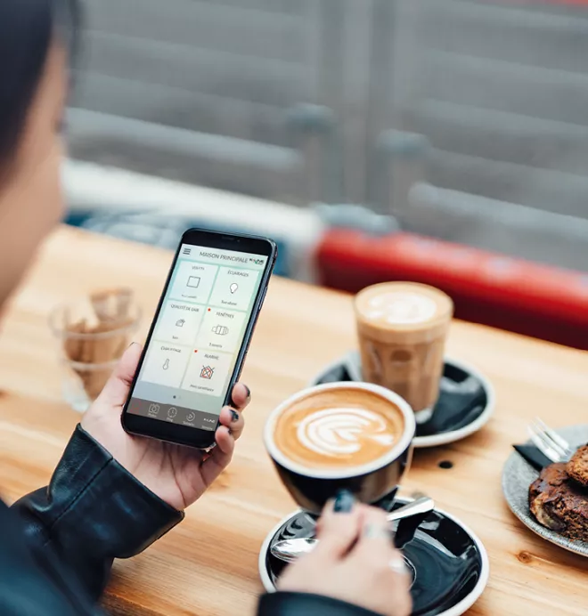 Une personne utilise un smartphone dans un café, tout en tenant une tasse de café avec de la nourriture sur la table.