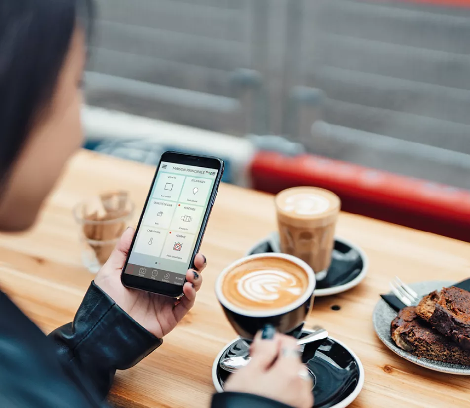 Une personne utilise un smartphone dans un café, tout en tenant une tasse de café avec de la nourriture sur la table.