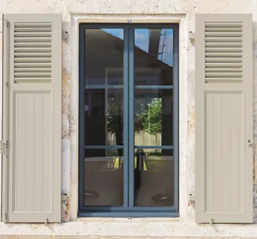 Fenêtre à deux battants, volets ouverts, encadrée par des murs en pierre, reflétant un jardin en arrière-plan.