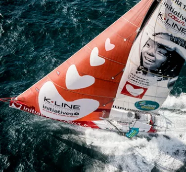 Voilier coloré avec des cœurs sur les voiles navigue en mer agitée, promouvant des initiatives charitables visibles sur la coque.