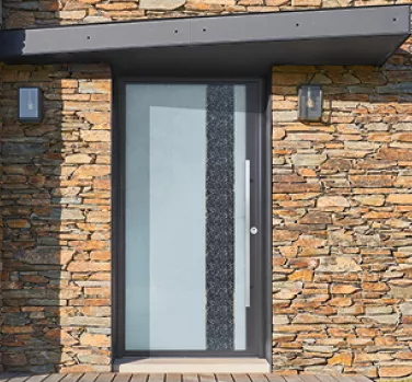 Porte moderne en verre dépoli avec bande décorative noire, encastrée dans un mur en pierre, éclairée par deux appliques murales.