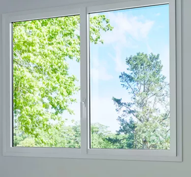 Fenêtre ouverte montrant des arbres verts et un ciel bleu, baignant la pièce de lumière naturelle.