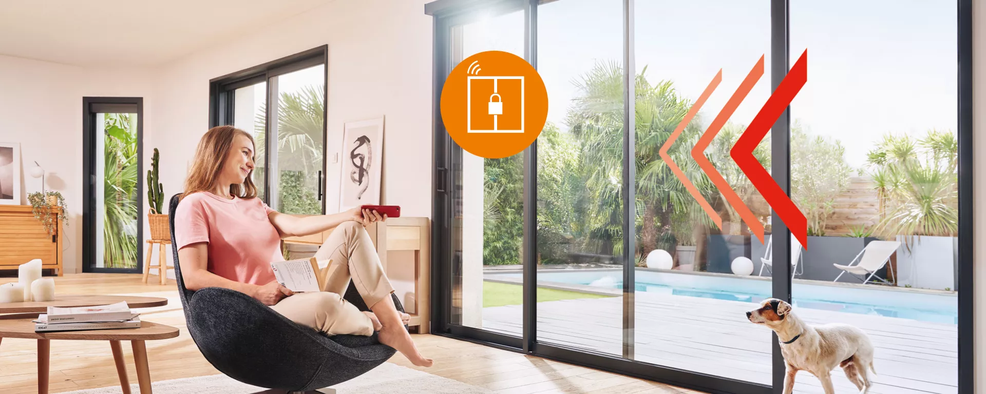 Femme, assise, utilise télécommande, contexte lumineux salon avec baies vitrées et piscine, chien en attente à l'extérieur.
