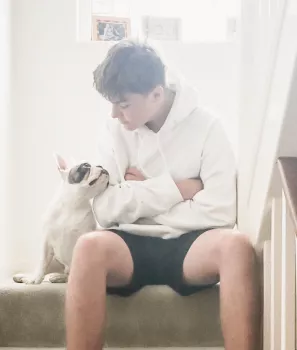 Un garçon assis sur les escaliers regardant un chien assis à ses côtés dans une maison bien éclairée.