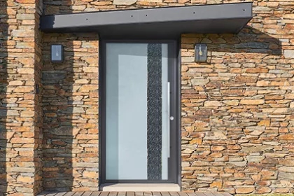 Porte moderne en verre dépoli avec bande décorative noire, encastrée dans un mur en pierre, éclairée par deux appliques murales.