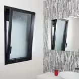 Fenêtre basculante noire s'ouvre dans une salle de bain moderne avec lavabo, miroir et carreaux muraux à motifs verticaux.